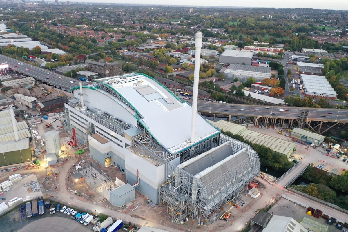 Aerial view of a modern industrial waste treatment facility with white buildings, tall smokestack, and surrounding urban residential areas